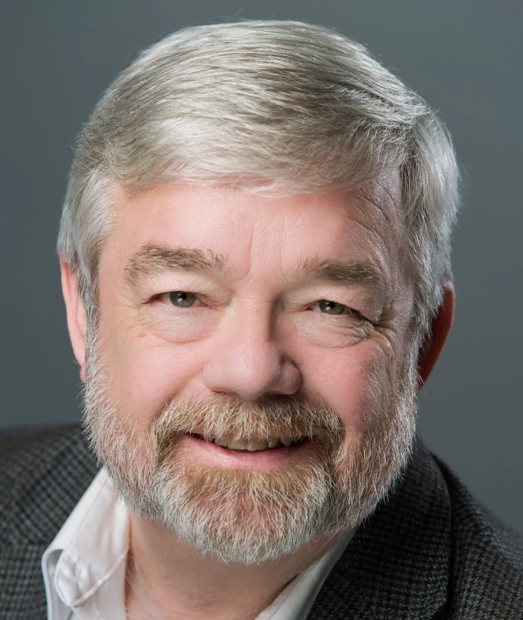 Smiling older man with gray hair and beard in professional portrait.