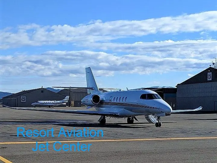 Private jet at airport with hangars visible.